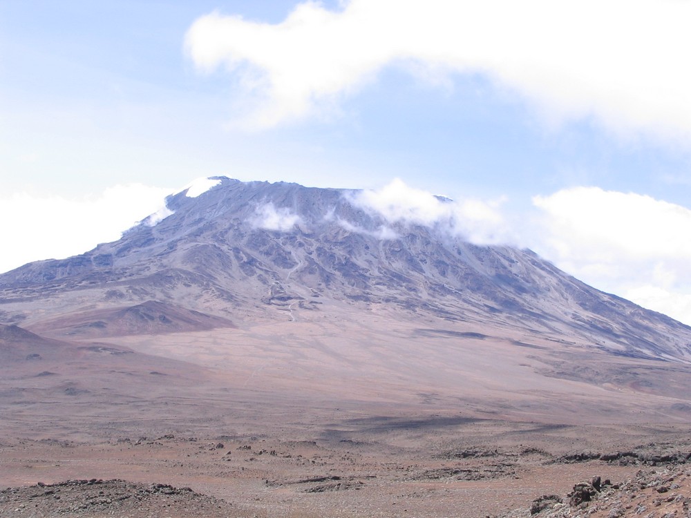 Panorama Kilimanjara sa Manenzija. Vidi se stazica od Kibo huta, uz sipar prema obodu kratera. Tuda se ide na vrh. Desno je Kenija. Granica ide podnožjem sa desne strane. To je i uzrok sukoba Kenije i Tanzanije. Kenija bi htela da bude njen. Dobar biznis. Hiljade zanešenih matoraca koji su odrasli uz film Lorensa Olivijea dolazio da vidi snegove na Kilimanjaru, ali odavde gledano više ga i nema.